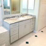 A bathroom with white cabinets and marble countertop.