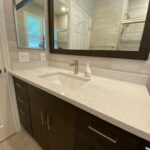 A bathroom with a white sink and mirror, featuring a bathroom cabinet for storage.