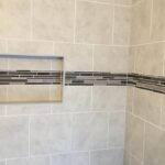 A tiled shower with a shelf and tiled walls in a bathroom design.
