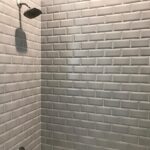 A white tiled shower with a white shower head in a bathroom design.