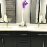 A bathroom with black cabinets and a purple flower. The bathroom cabinet blends seamlessly with the dark color scheme, providing ample storage space for all your toiletries. As you enter the bathroom, your