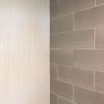 A bathroom with a grey tiled wall and shower.