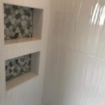 A white tiled shower with a tiled shelf in a bathroom design.