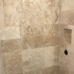 A beige tiled shower with a beige tiled floor.