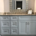 A bathroom remodel featuring gray cabinets and a mirror.