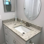 A bathroom with granite counter tops, a mirror, and a bathroom cabinet.