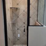 A shower with a glass door and tiled floor in a bathroom remodel.