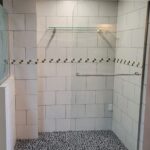 A bathroom with a glass shower door and tiled floor, showcasing a modern bathroom design.