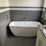 A bathroom with a white bathtub and gray tile.
