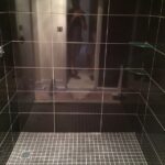 A stylish bathroom design featuring a black tiled shower with a person standing in it.