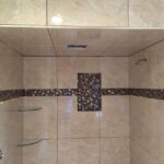A shower with beige tile and a glass shelf, perfect for a modern bathroom design.