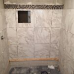 A bathroom remodel includes tiling the walls and floor with marble tiles.