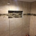 A beige tiled shower with a tiled wall.