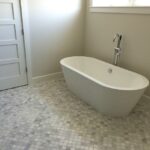 A white bathtub in a bathroom with a white tile floor. The minimalist bathroom design boasts a sleek bathtub that seamlessly blends with the pristine tile floor.