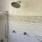 A glass shower head in a white tiled shower.
