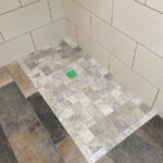 A tiled shower with a green tile on the floor and a bathroom cabinet.