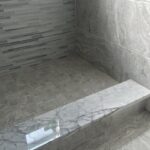 A gray tiled shower with a marble floor. The bathroom remodel features a sleek and modern look, with a focus on the stunning shower design.