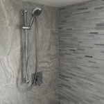 A stylish shower with a grey tiled wall and shower head, showcasing an impeccable bathroom design.