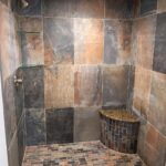 A shower with brown tile and a granite bench in a bathroom design.