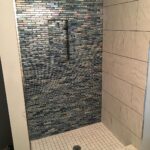 A blue tiled shower with a tiled floor.