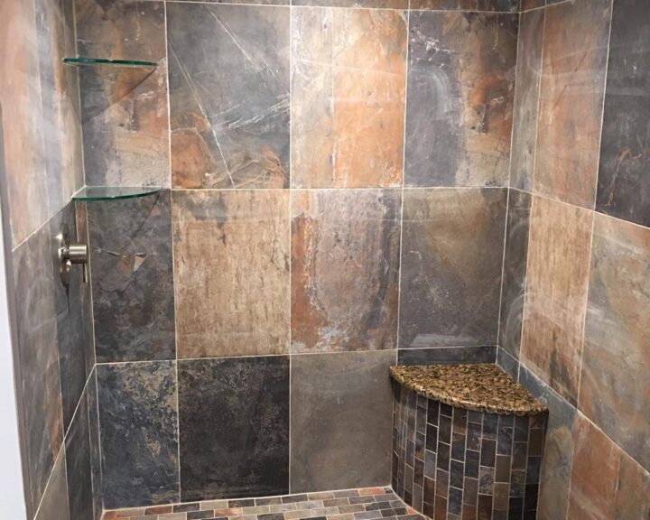 A shower with brown tile and a granite bench in a bathroom design.